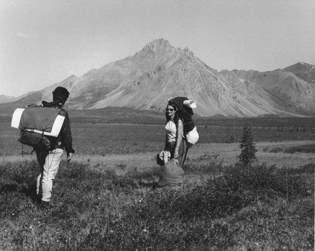 Two people with hiking gear, standing at the foot of a mountain