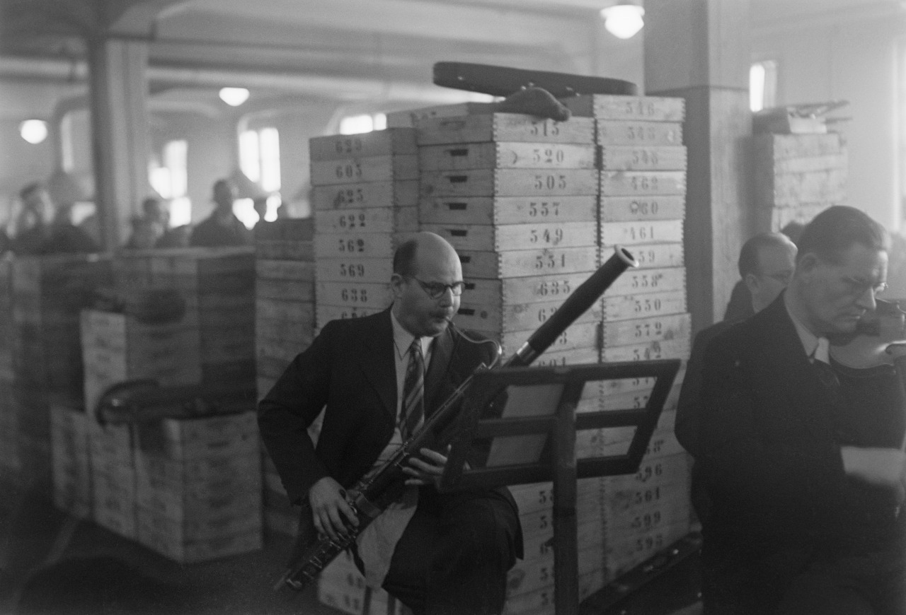 A suited man playing the bassoon in a factory setting